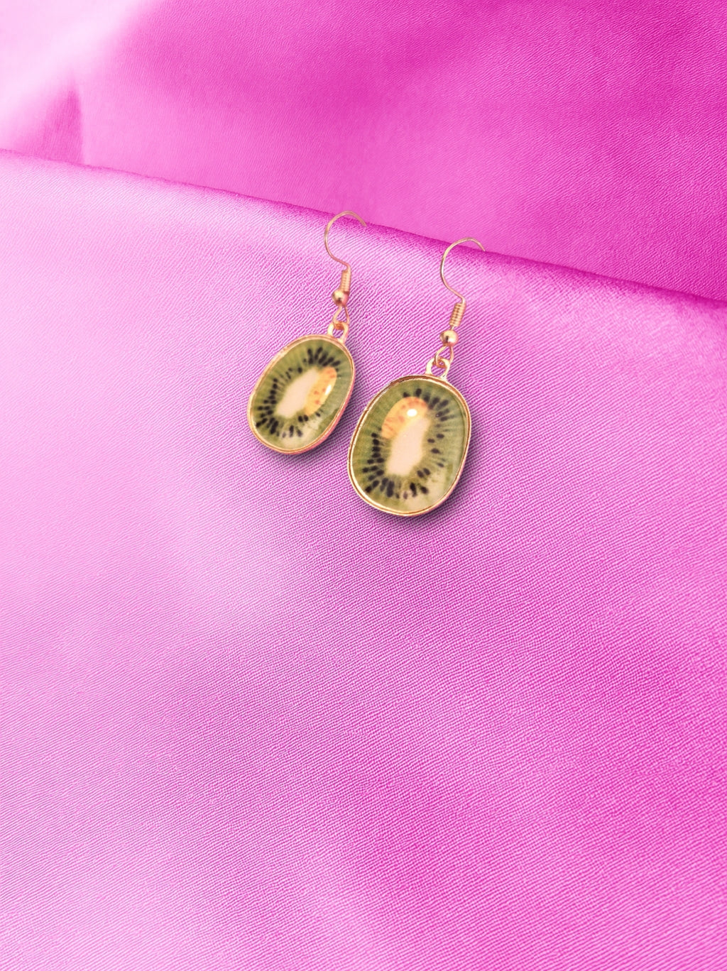 Kiwi fruit-shaped earrings on a pink fabric background