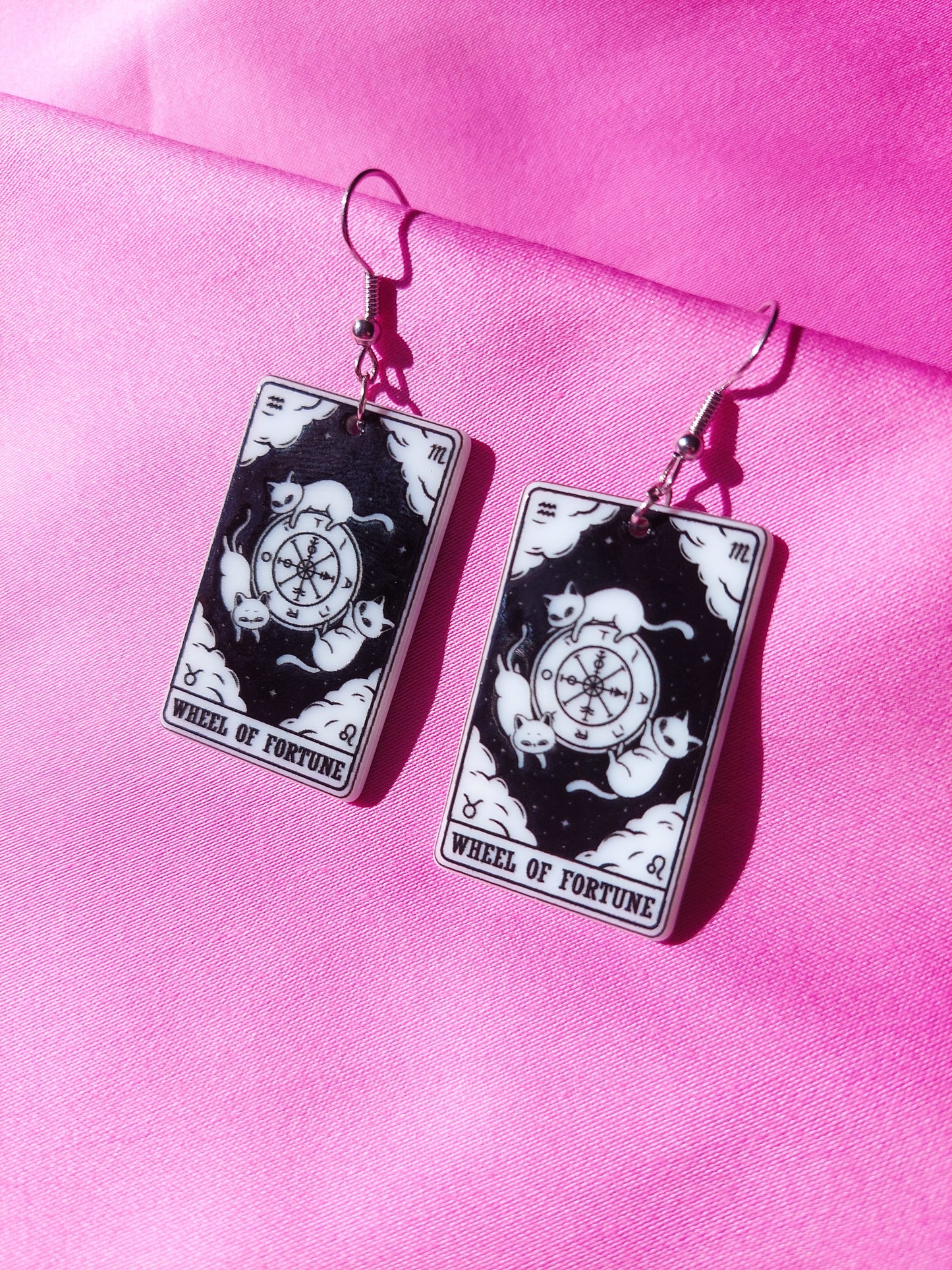Tarot earrings that are black and white on a pink background