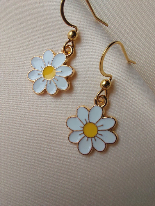 White petal flower earrings with yellow centre. Gold trim around outside of flower. Gold Hooks. Earrings laid on fabric.