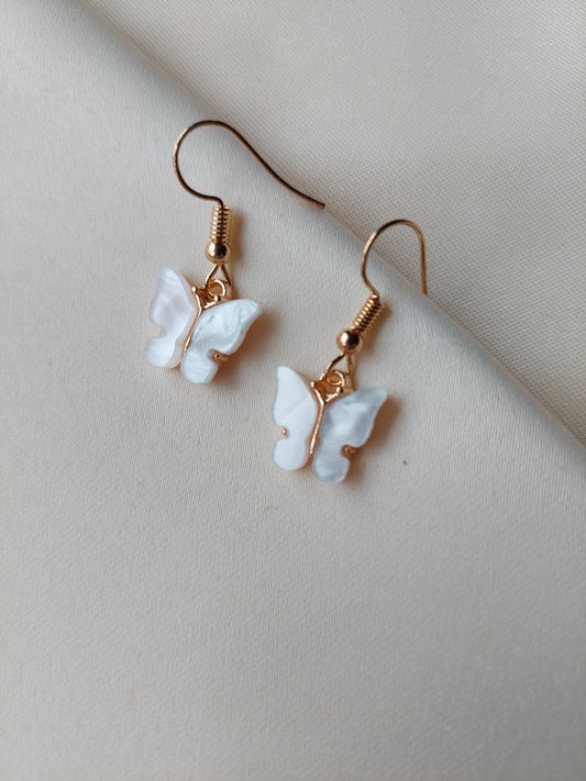 White butterfly earrings with gold body. Gold hooks placed on fabric.