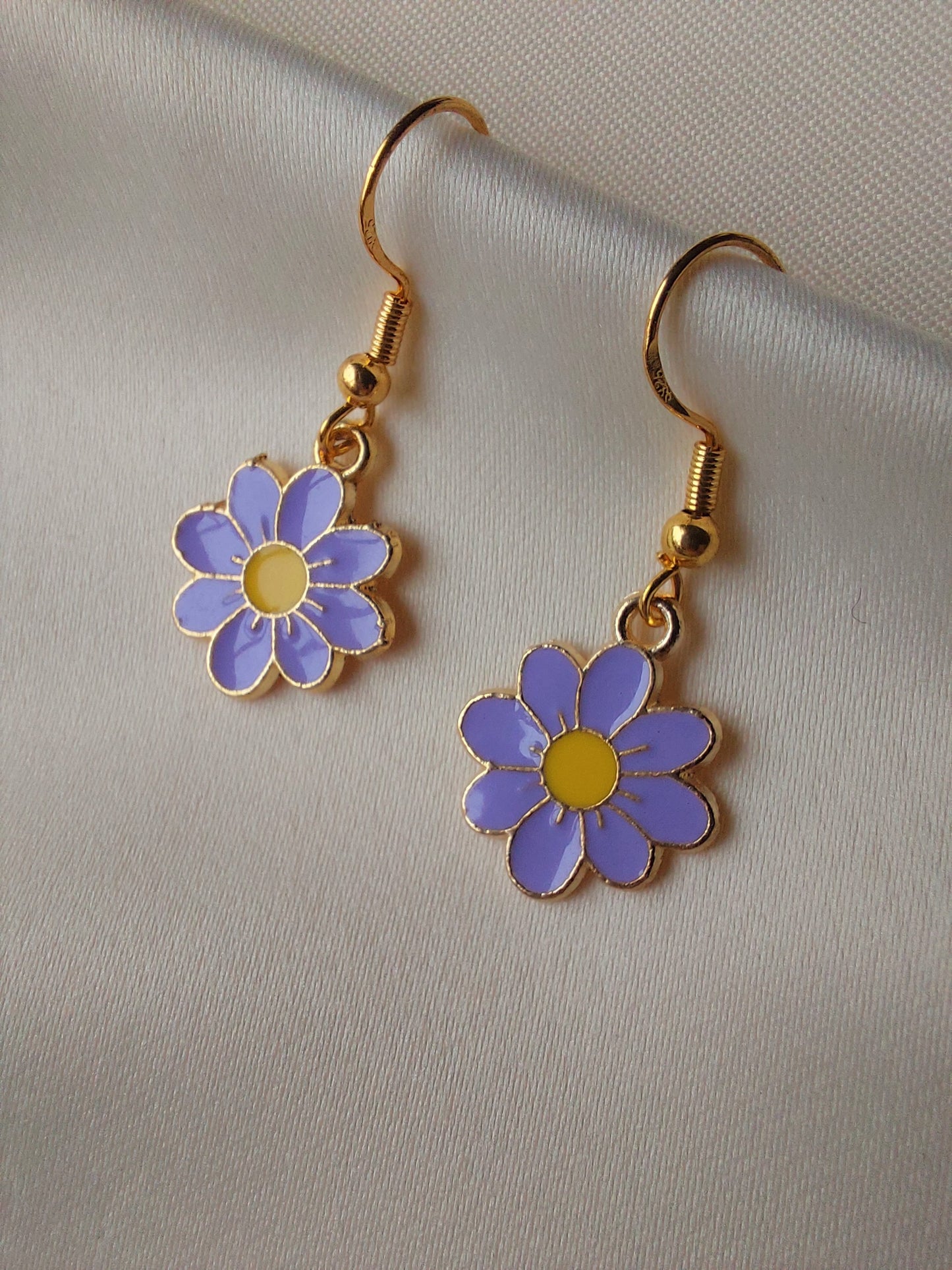 Light purple petal flower earrings with yellow centre. Gold trim around outside of flower. Gold Hooks. Earrings laid on fabric.