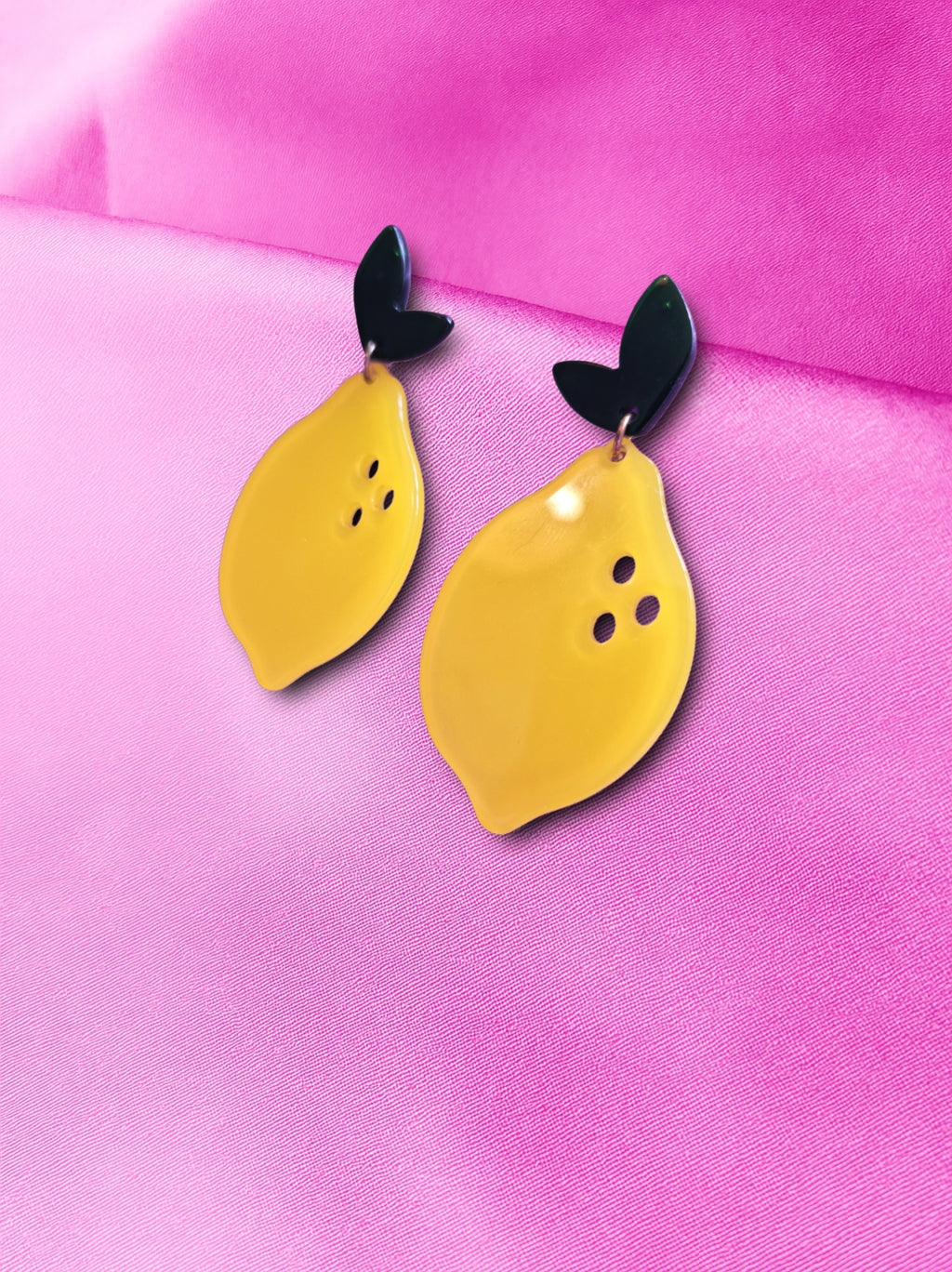 Yellow lemon-shaped earrings with green accents on a pink background