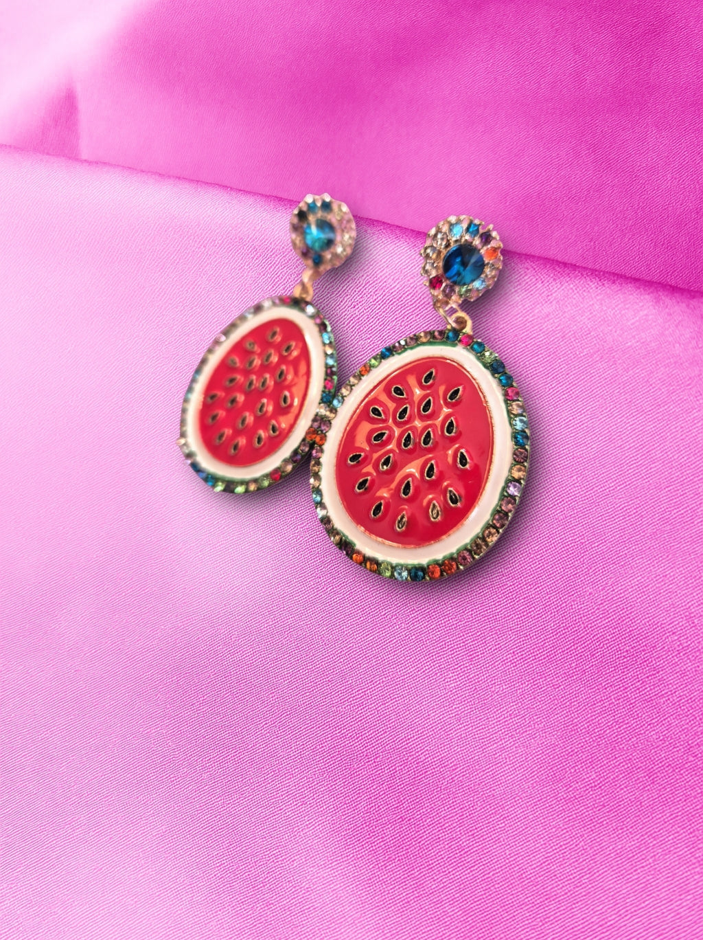 Watermelon-themed earrings with gemstones on a pink background