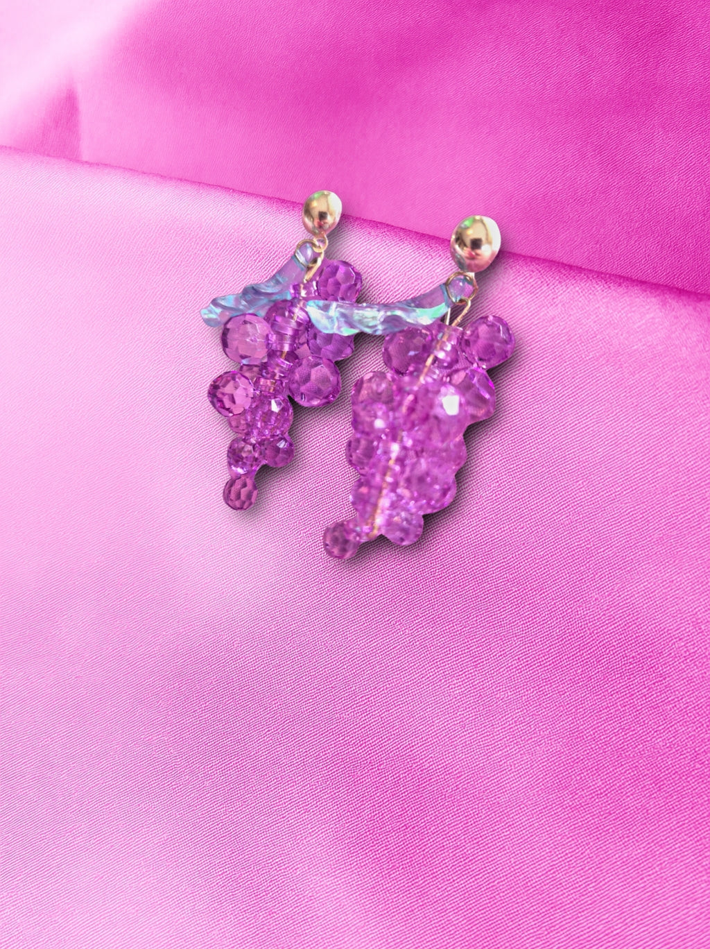 Purple grape-shaped earrings on a pink fabric background