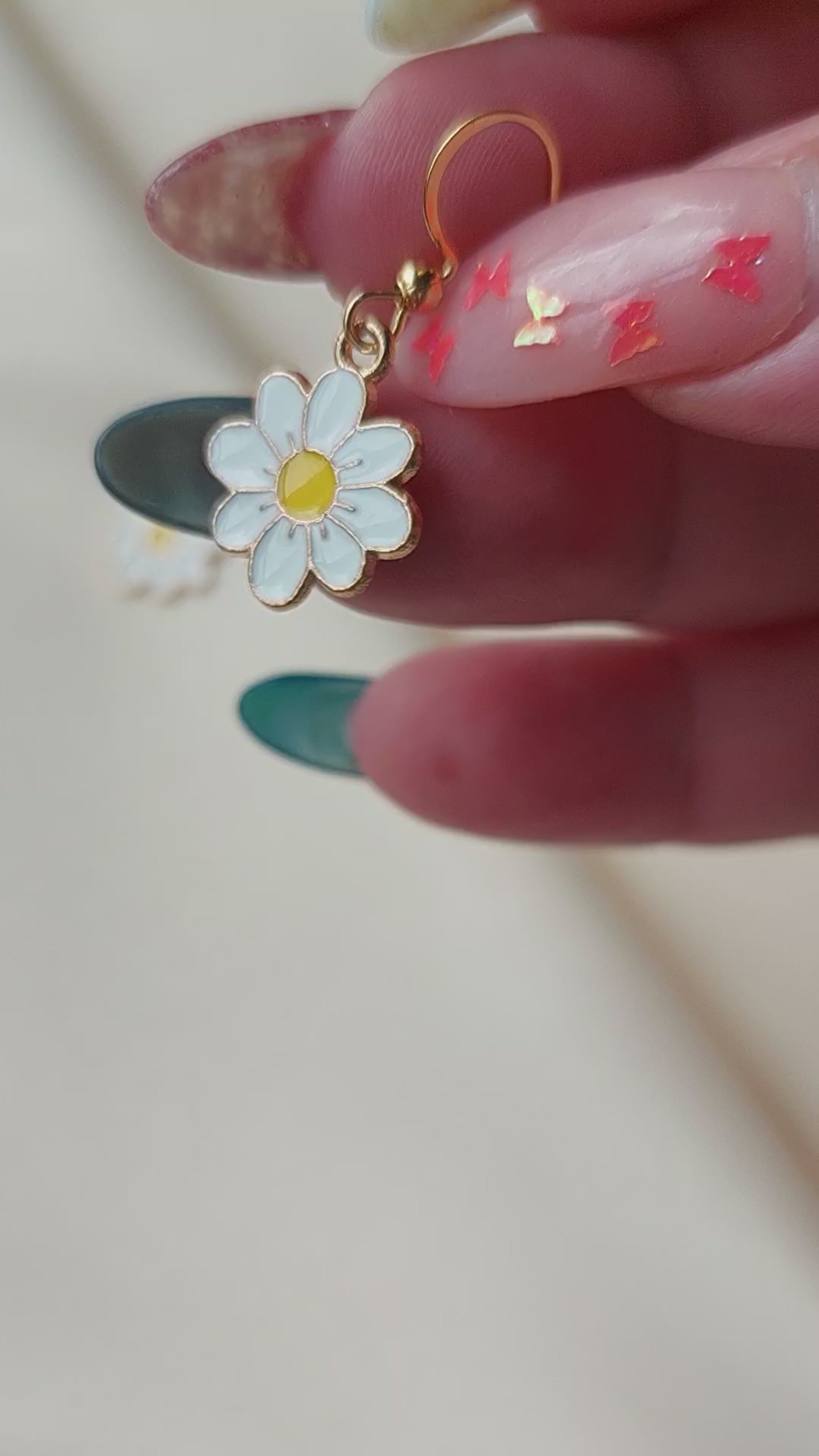 White petal flower earrings with yellow centre. Gold trim around outside of flower. Gold Hooks. Earrings laid on fabric.  Held in hand for size comparison. 