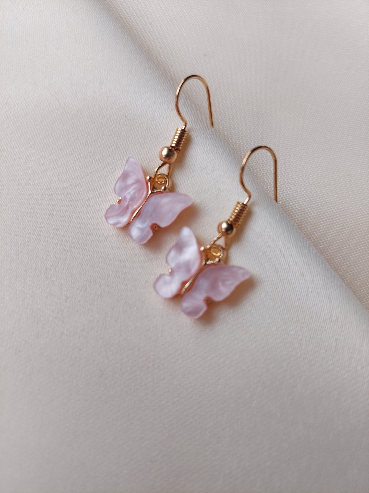 Light pink butterfly earrings with gold body. Gold hooks placed on fabric. 