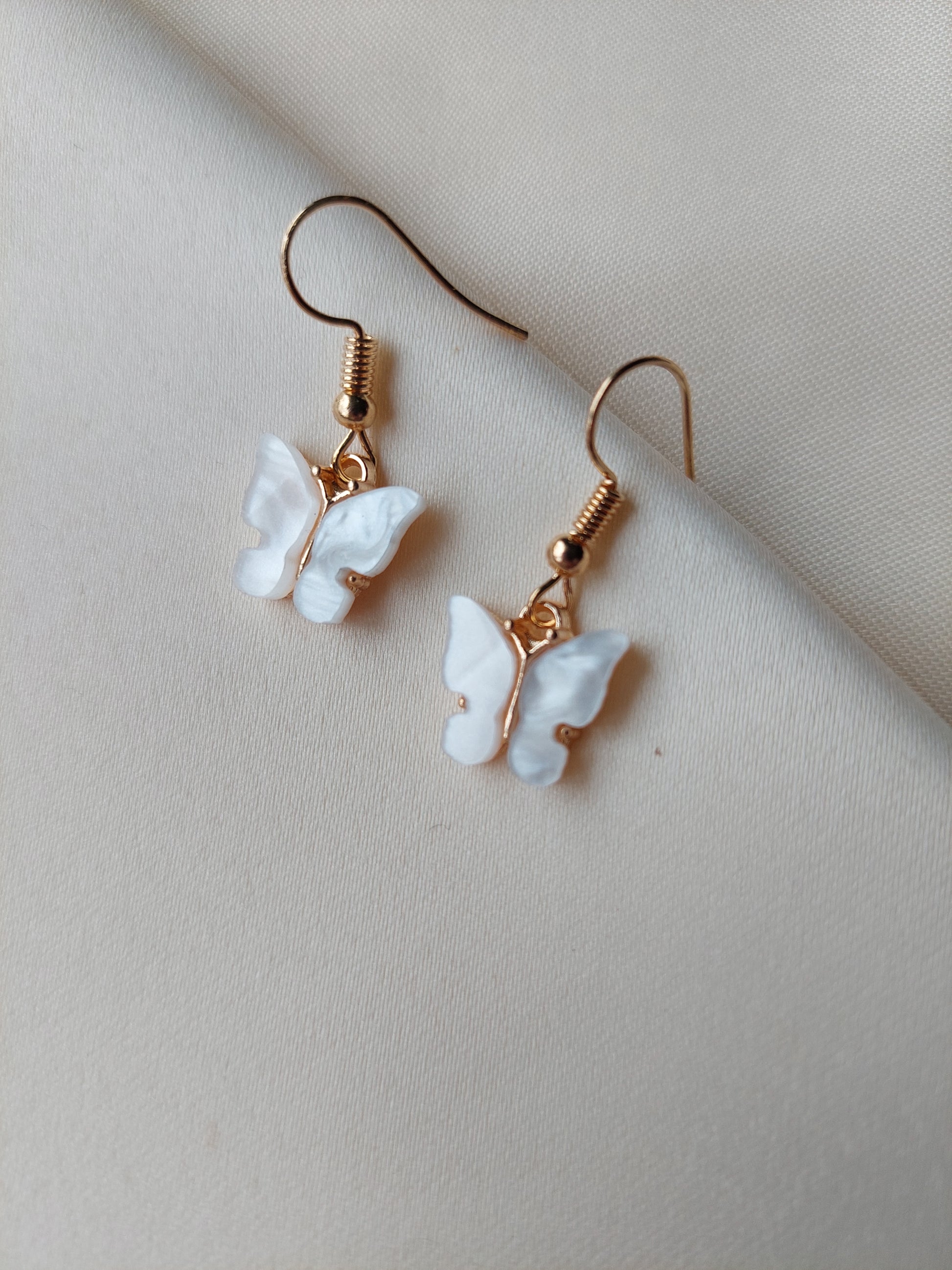 White butterfly earrings with gold body. Gold hooks placed on fabric. 