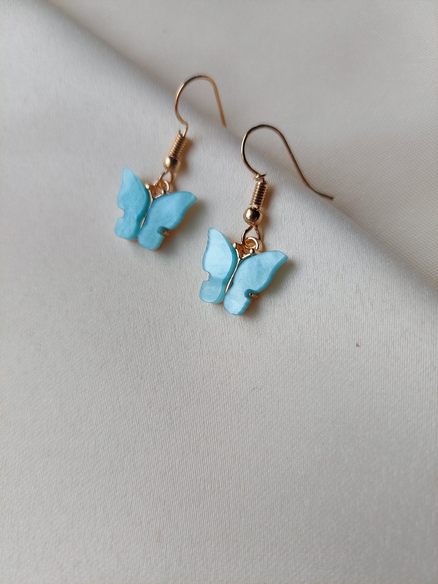 Light blue butterfly earrings with gold body. Gold hooks placed on fabric. 