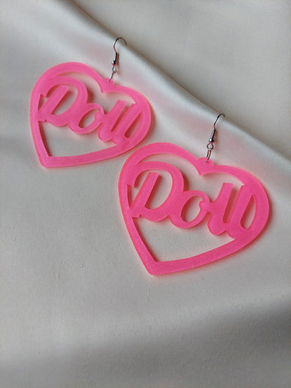 Bright pink heart shaped earrings with doll lettering in the middle of the heart. Silver earring hooks in the middle of the heart. Pink include some glitter throughout it. 