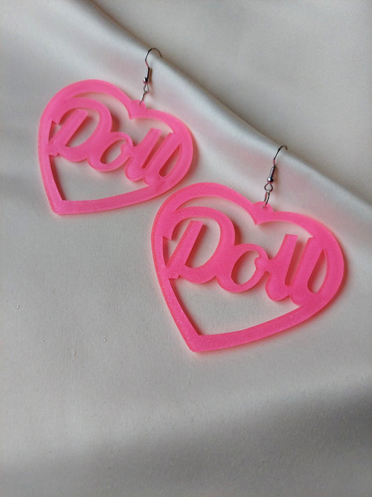 Bright pink heart shaped earrings with doll lettering in the middle of the heart. Silver earring hooks in the middle of the heart. Pink include some glitter throughout it. 