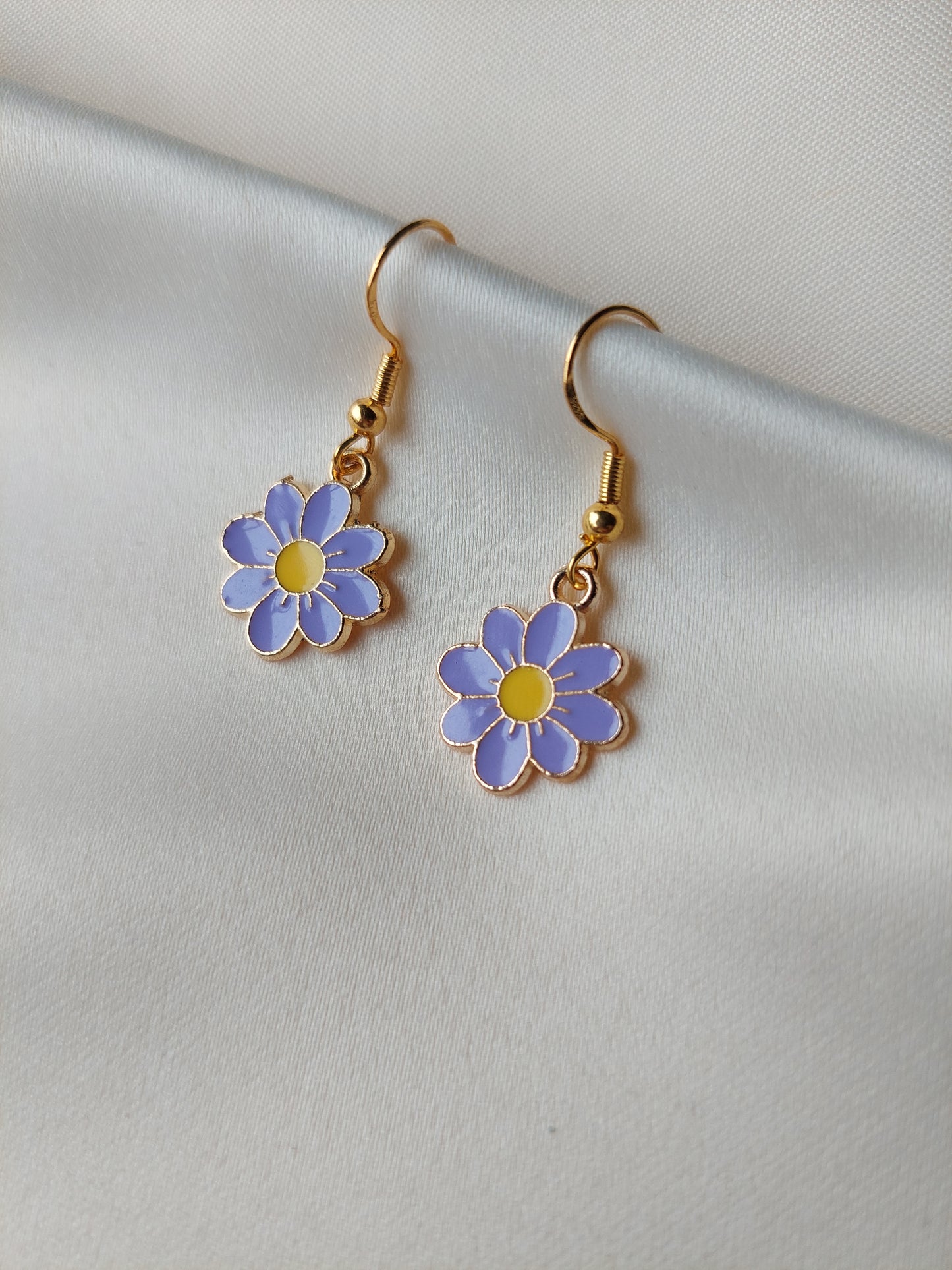 Light purple petal flower earrings with yellow centre. Gold trim around outside of flower. Gold Hooks. Earrings laid on fabric. 