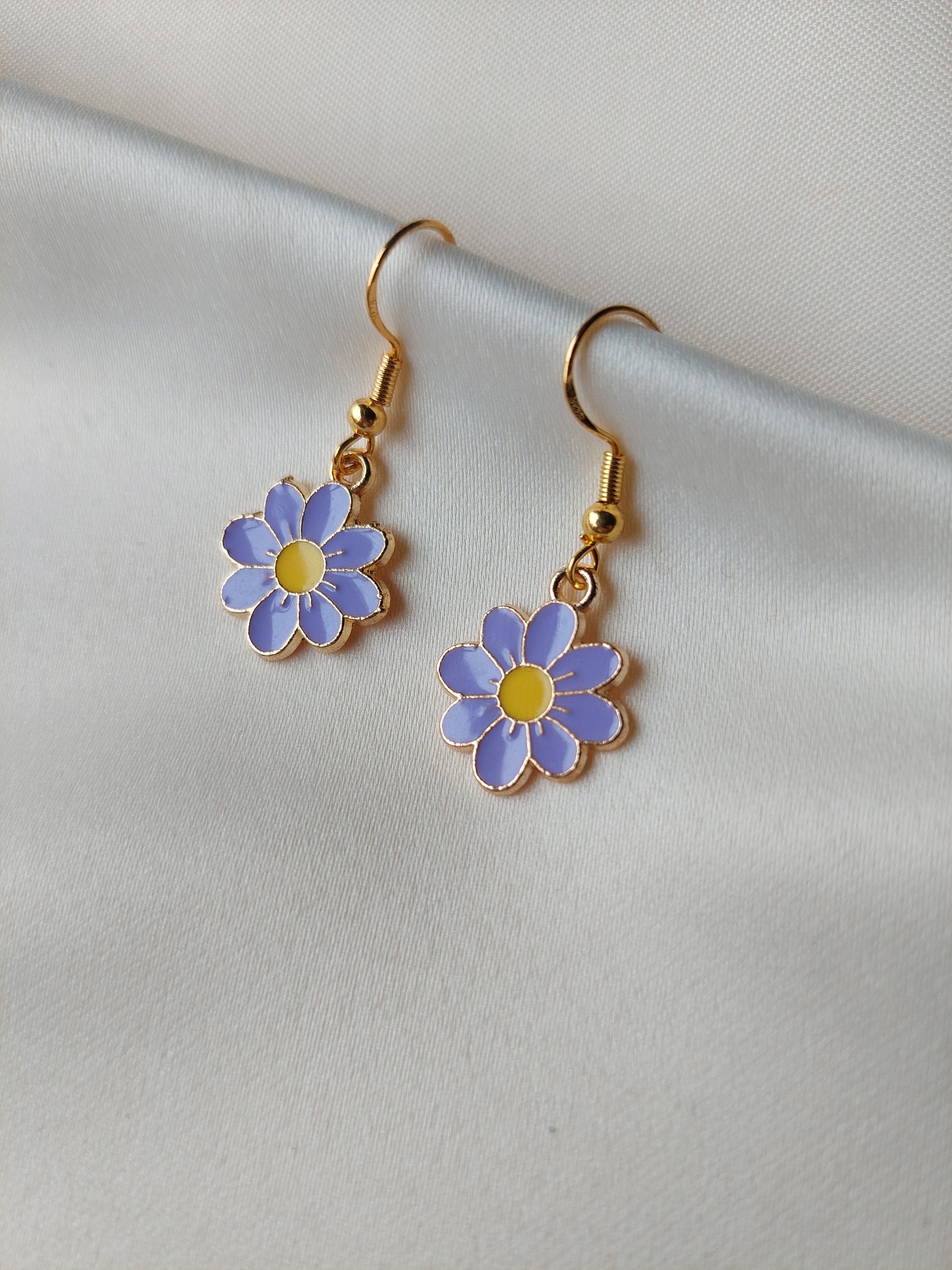 Light purple petal flower earrings with yellow centre. Gold trim around outside of flower. Gold Hooks. Earrings laid on fabric. 