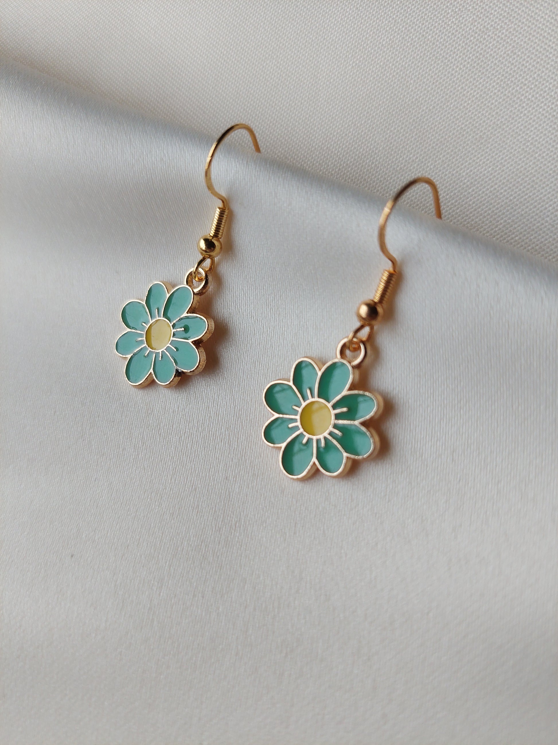 Green petal flower earrings with yellow centre. Gold trim around outside of flower. Gold Hooks. Earrings laid on fabric. 