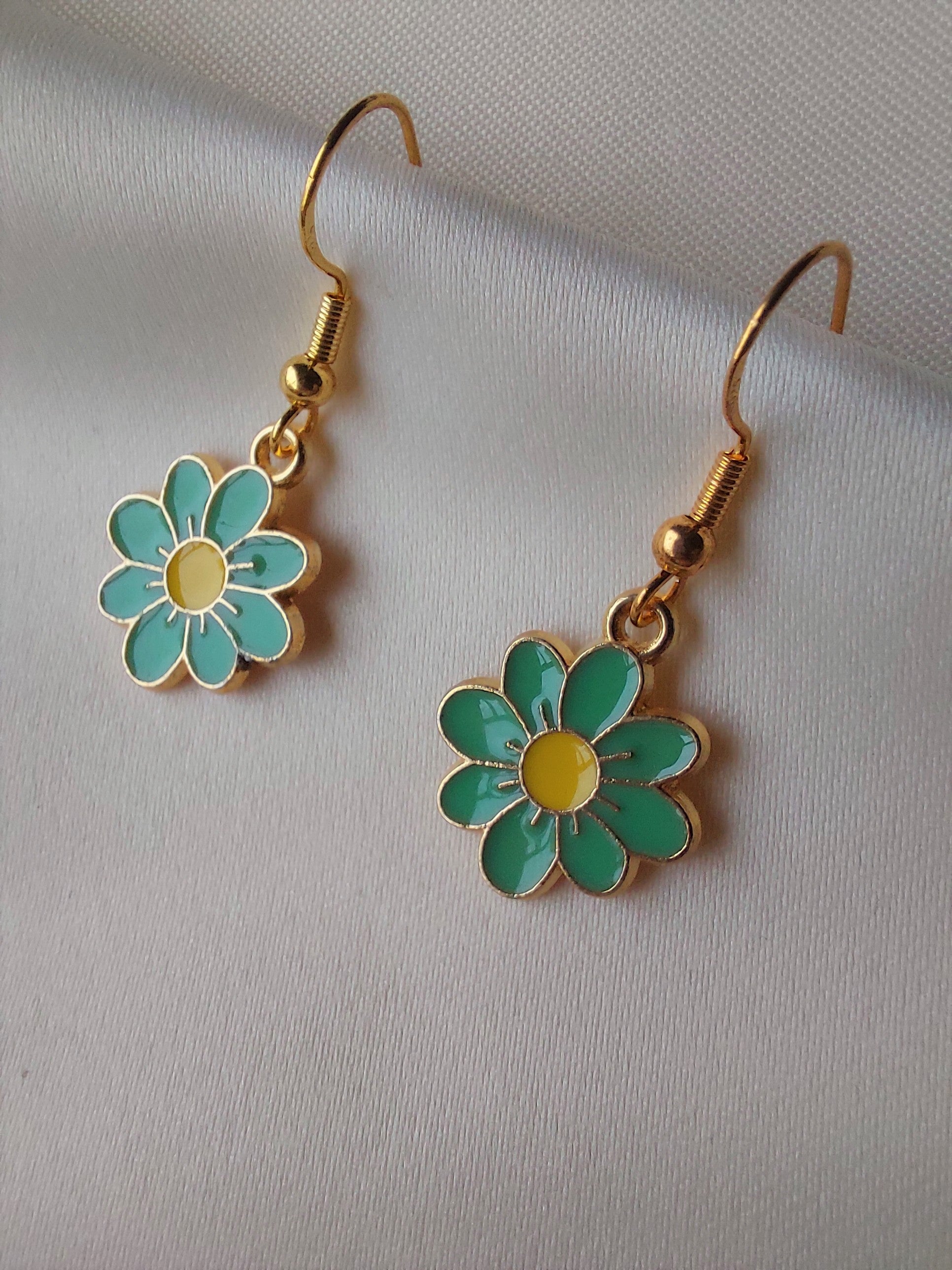 Green petal flower earrings with yellow centre. Gold trim around outside of flower. Gold Hooks. Earrings laid on fabric.