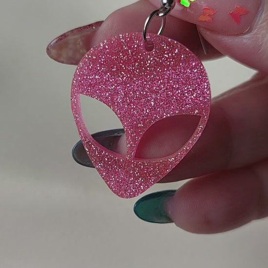 Pink glitter alien head earrings. Hanging on with silver earring hooks. Hand included for size comparison.