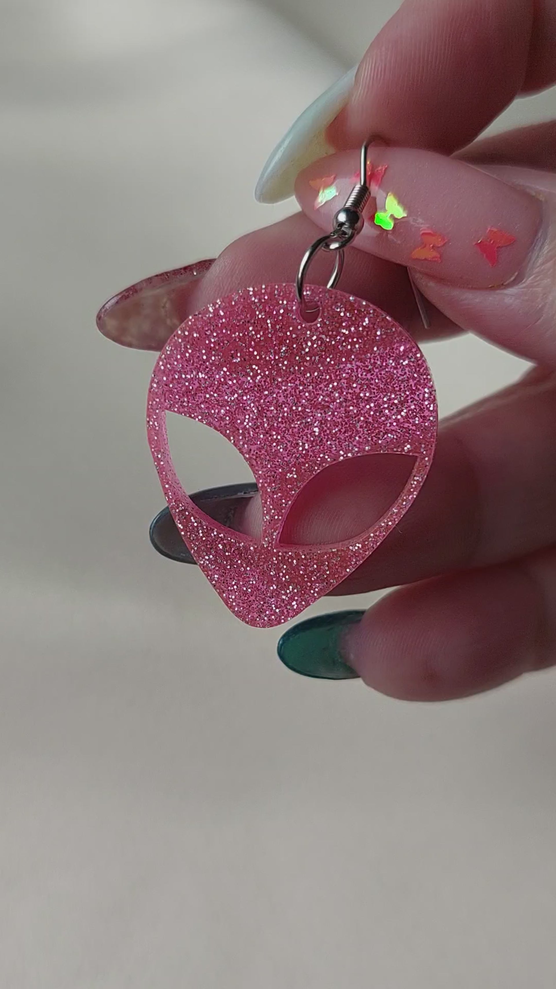 Pink glitter alien head earrings. Hanging on with silver earring hooks. Hand included for size comparison.