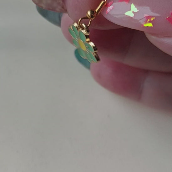 Green petal flower earrings with yellow centre. Gold trim around outside of flower. Gold Hooks. Earrings laid on fabric. Held in hand for size comparison.
