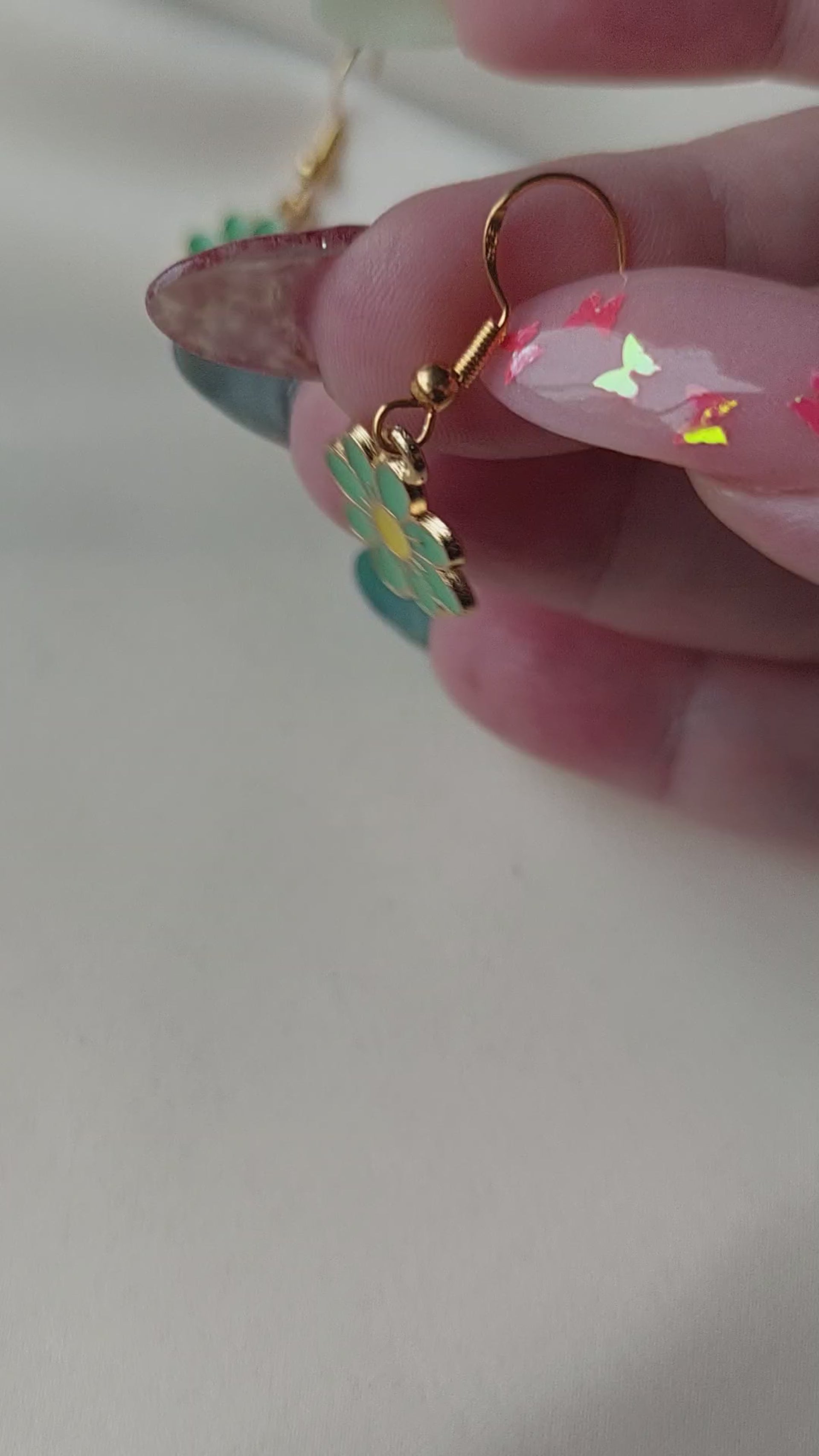 Green petal flower earrings with yellow centre. Gold trim around outside of flower. Gold Hooks. Earrings laid on fabric. Held in hand for size comparison.