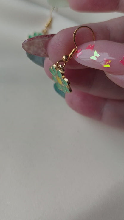 Green petal flower earrings with yellow centre. Gold trim around outside of flower. Gold Hooks. Earrings laid on fabric. Held in hand for size comparison.