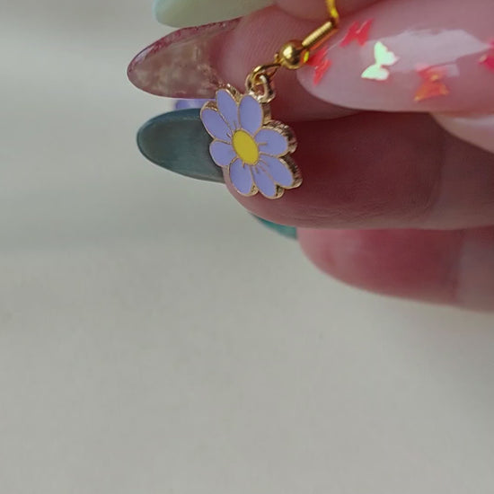 Light purple petal flower earrings with yellow centre. Gold trim around outside of flower. Gold Hooks. Earrings laid on fabric. 