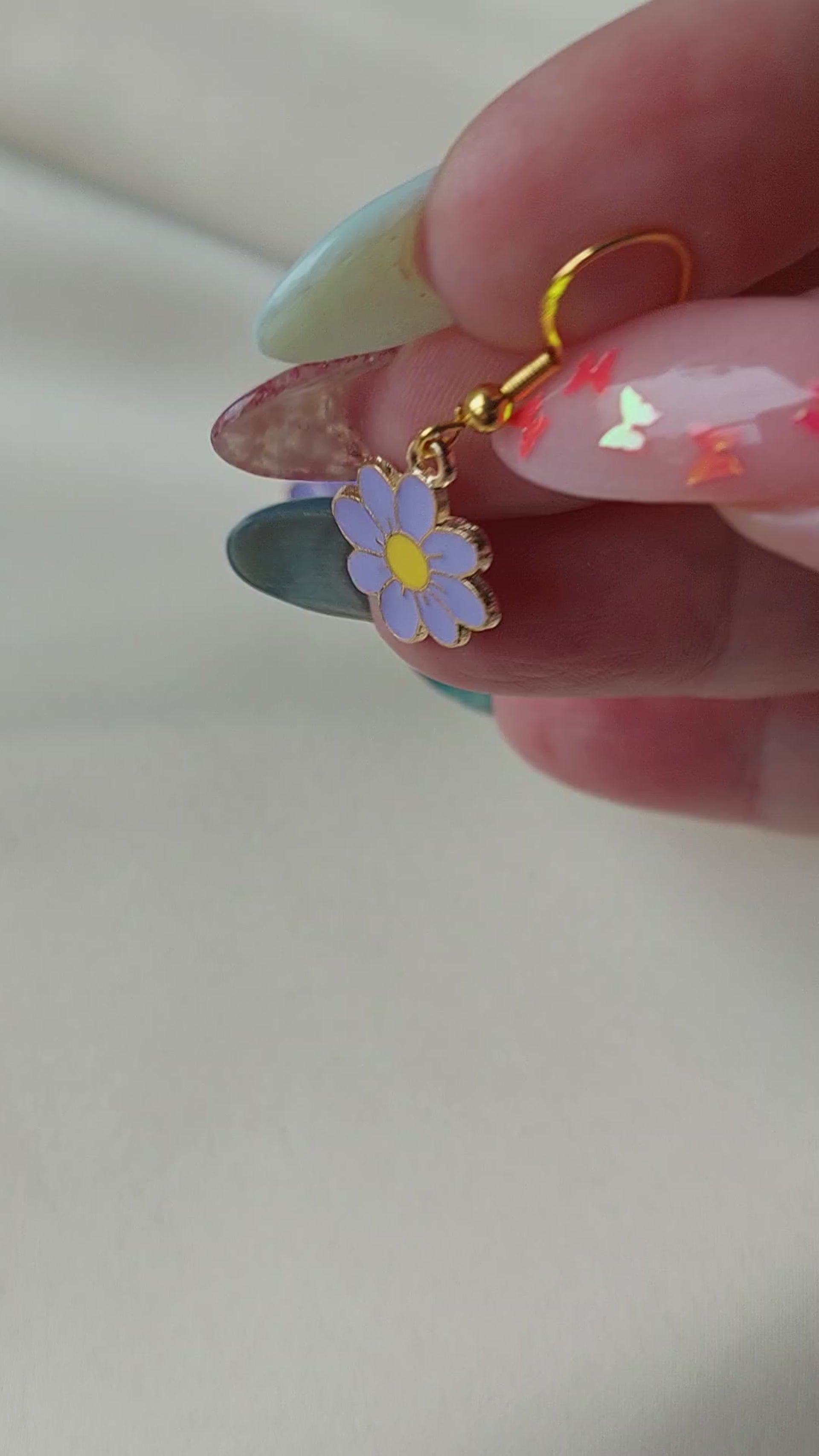Light purple petal flower earrings with yellow centre. Gold trim around outside of flower. Gold Hooks. Earrings laid on fabric. 